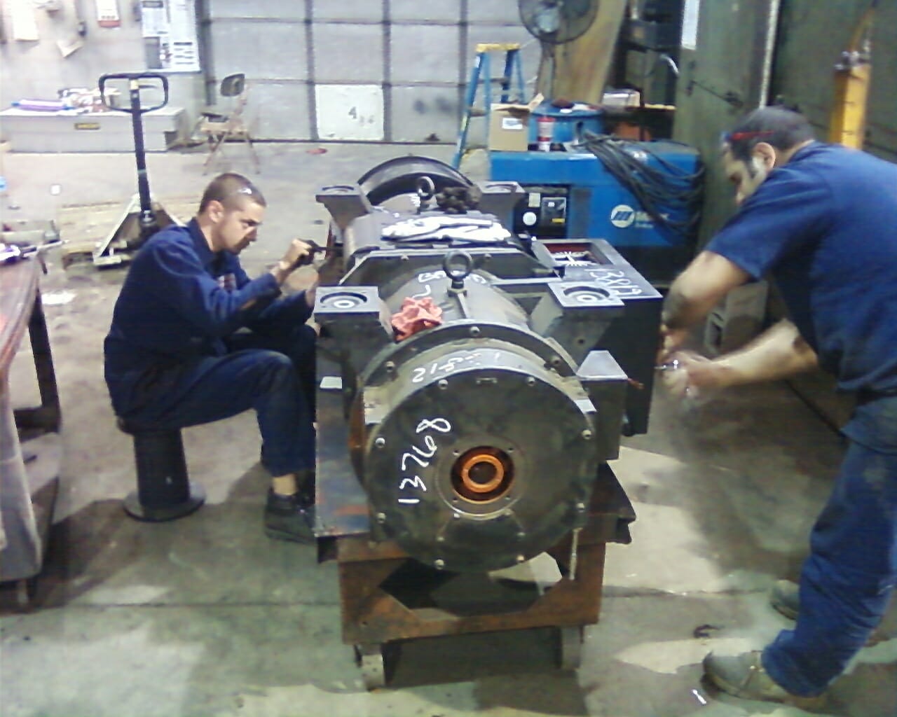 two technicians repairing a motor alternator unit.