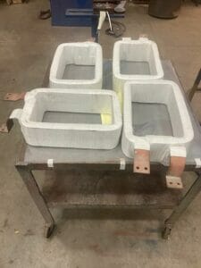 Four rectangular-shaped reinsulated DC coils on a rolling machine shop cart